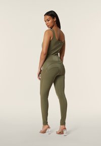 Completo activewear verde oliva composto da una top senza maniche e leggings aderenti. Tessuto liscio, design scolpito e dettagli di branding minimi visibili.
