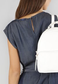 Top in denim a maniche corte con chiusura sul retro; zaino in pelle bianca con tasca con zip e tracolla decorata con catena.