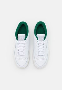 Zapatillas de piel blanca con interior verde, con puntera redonda, cordones y detalles perforados en los laterales. Toque de crema en la suela.