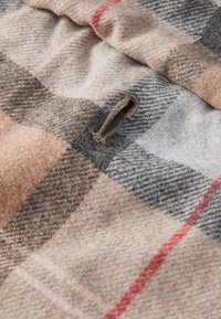 Close-up of beige, gray, and red plaid wool fabric with a vertical buttonhole stitched along the edge.