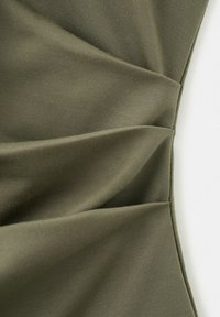 Tissu vert olive avec des plis diagonaux et des coutures, montrant la texture et les plis sur une surface textile lisse.