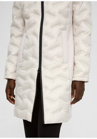 Leichte, gesteppten Pufferjacke in sanftem Creme mit einem durchgehenden Reißverschluss, kontrastierenden dunklen Akzenten und seitlichen Taschen. Texturiertes, isoliertes Design.