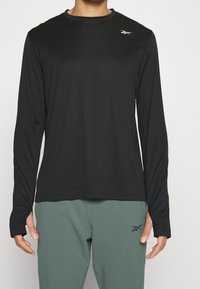 Svart långärmad träningströja med rund halsringning, tillverkad av lätt material. Har en liten logotyp på bröstet och tumhål i ärmarna.