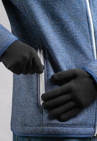 Veste texturée bleue avec une poche zippée gris-noir. Des gants en tricot noirs sont portés, gripant l'ouverture de la poche. Des poignets bleus accentuent les manches.