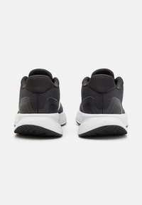Paire de chaussures de sport noires et blanches vues de dos, avec talons rembourrés et semelles blanches texturées sur un fond uni.