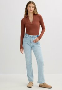 Top de manga larga en color óxido con diseño de canalé y escote en V, combinado con jeans rectos de color azul claro y zuecos color tostado con suela texturizada.