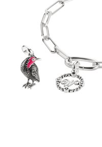 Silbernes Gliederarmband mit einem schwarzen Vogelanhänger mit roten Akzenten und einem runden Anhänger mit eingraviertem Buchstaben und Perlendetails.