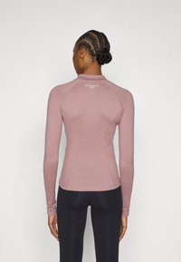 Fitted long-sleeve top in muted pink, made from stretch fabric. Features a high neckline and back logo. Smooth texture and raglan sleeves.