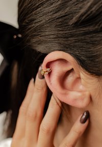 Gold Ohrcuff mit zwei bunten Edelsteinen, der eng am oberen Ohr sitzt. Die glatte Metalloberfläche harmoniert mit dem Hautton und der Haarstruktur.