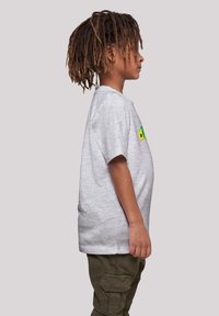 Camiseta gris de manga corta con cuello redondo, que presenta un parche gráfico colorido en el pecho. Combinada con pantalones cargo verdes.