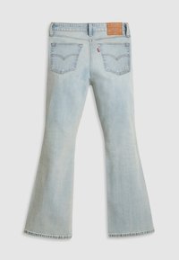 Jean flare en denim bleu clair à taille haute, avec une étiquette en cuir à l'arrière de la taille, et deux poches arrière avec des détails de couture.