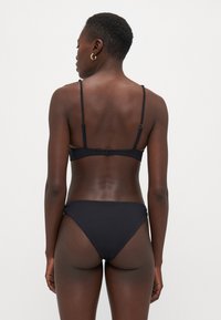 Fekete bikini szett, egyszerű dizájnnal, állítható pántokkal, hátul kapcsos záródással és magas szabású alsó résszel. Simább textúrájú.