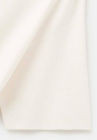 Tessuto a maglia color crema con una texture liscia, caratterizzato da un design semplice e una cucitura pulita lungo il bordo.