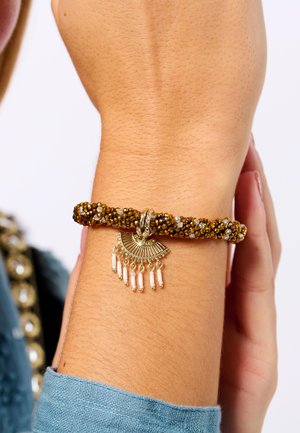Bracelet en perles avec un fermoir en métal doré, comportant un charme en forme d'éventail décoratif et des perles blanches suspendues. Perles de couleur marron et ambre.