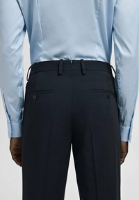 Jasnoniebieska koszula z długim rękawem, zestawiona z ciemnymi, dopasowanymi spodniami z tylnymi kieszeniami o gładkiej fakturze.