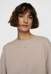 Lichtbeige trui met een ronde halslijn, verlaagde schouders en een textuuraccent bij de kraag. Glad materiaal met een ontspannen pasvorm.