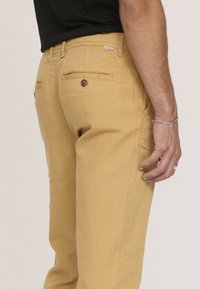Pantalon en coton jaune à coupe droite, doté de deux poches arrière, d'une fermeture à bouton marron et d'un accent logo subtil près de la taille.