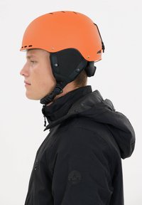 Orange hjelm med ventilationshuller og justerbare stropper, kombineret med en sort jakke med hætte og logo på ærmet.