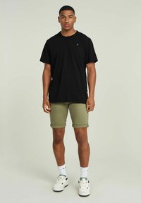 Czarny bawełniany t-shirt z krótkim rękawem, oliwkowe, podwinięte szorty, białe trampki i skarpetki do kostek. Prosty design z minimalnym logo.