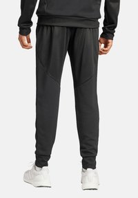 Zwarte sportbroek met een gematteerde afwerking, voorzien van een aansluitende pasvorm, paneeldetails en een elastische tailleband, gecombineerd met witte sneakers.
