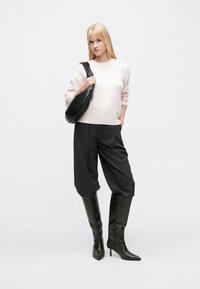 Παστέλ ροζ πουλόβερ με κατεβασμένους ώμους, γκρι πλισέ παντελόνι και μαύρες μπότες μέχρι το γόνατο με μυτερή μύτη. Μαύρη τσάντα ώμου.