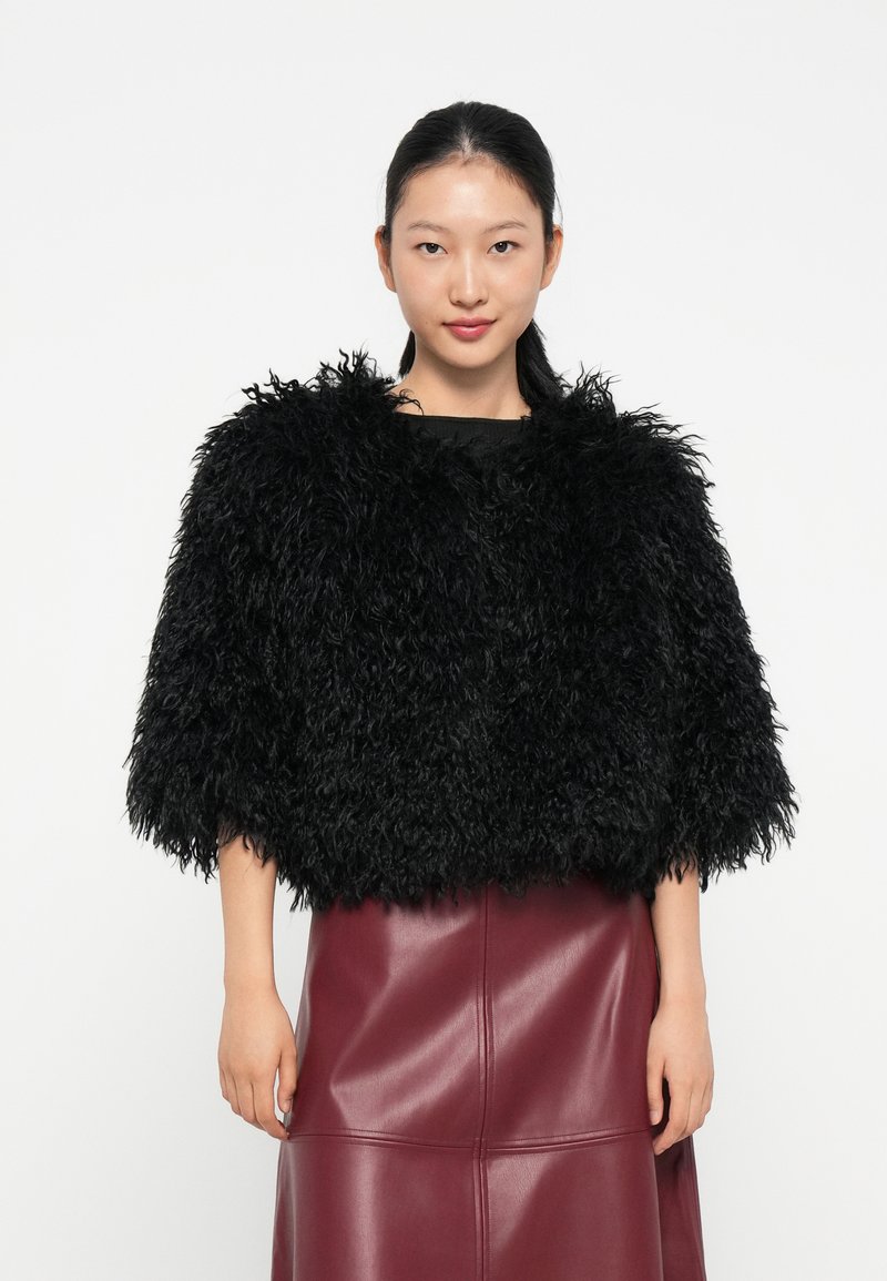 Veste noire en fausse fourrure courte avec un col haut, des manches courtes et une surface texturée, assortie d'une jupe en cuir ajustée bordeaux.