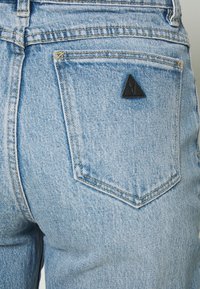 Vaaleansiniset farkut, joissa on kolmionmuotoinen musta lappu takataskussa, esittelevät teksturoitua kangasta ja klassisia muotoiluelementtejä.