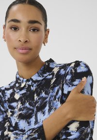 Camicia con bottoni caratterizzata da un motivo astratto blu e nero, con colletto classico e maniche lunghe. Tessuto liscio con una leggera lucentezza.