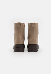 Béžové kožené kotníkové boty se zlatými zipy, texturovaným povrchem a tmavě hnědými robustními podrážkami. Boční švy zdůrazňují design.