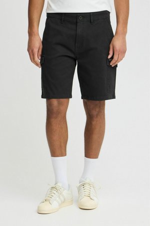 Schwarze Cargo-Shorts aus Baumwolle, mit Seitentaschen, einem Knopfverschluss und einem bequemen Sitz, kombiniert mit weißen Socken und Turnschuhen.