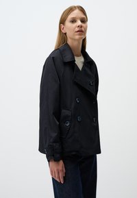 Granatowy płaszcz trench dwurzędowy z szerokim kołnierzem, z guzikami i swobodnym krojem, uszyty z gładkiego, lekkiego materiału.