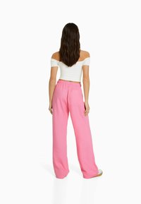 Pantalones de pierna ancha rosas con una cinturilla elástica y detalle de bolsillos. Combinados con un top corto de rayas blanco, sin mangas. Textura suave.