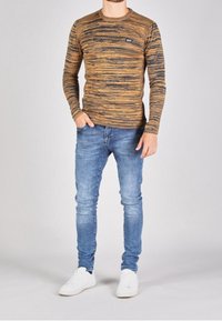 Sweter z długim rękawem w paski w ciepłych odcieniach brązu i czerni, połączony z niebieskimi dżinsami i białymi trampkami. Swobodny, dopasowany krój.