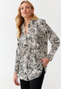 Lange mouwen button-up shirt in crème met een zwart abstract bladerenpatroon, met een kraag en een rechte snit, gedragen met zwarte broek.