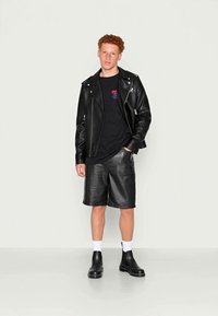 Svart skinnbikerjakke over en svart t-skjorte, parret med svarte skinnshorts og svarte ankelstøvler, båret med hvite sokker.
