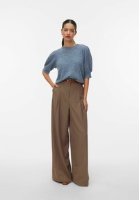 Jasnoniebieski, teksturowany sweter z krótkim rękawem, zestawiony z brązowymi, szerokimi spodniami z wysokim stanem oraz brązowym paskiem. Obuwie w kolorze brązowym.