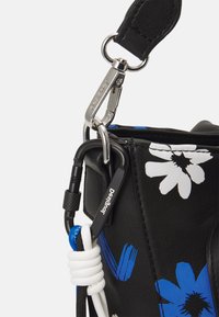 Schwarze Ledertasche mit blauen und weißen Blumenmotiven, ausgestattet mit Metallkarabinern und einem strukturierten Schulterriemen.