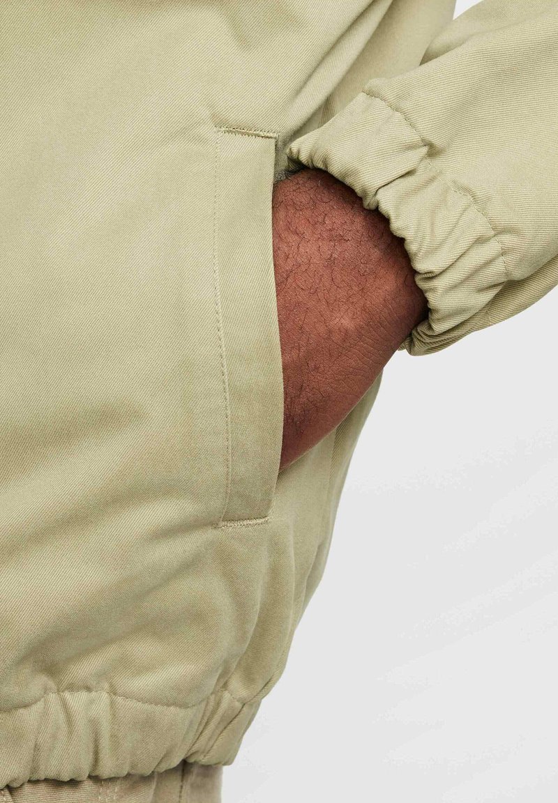 Chaqueta de un suave verde oliva con puños acanalados y un bolsillo lateral invisible, fabricada con un tejido liso y duradero, con un corte relajado.