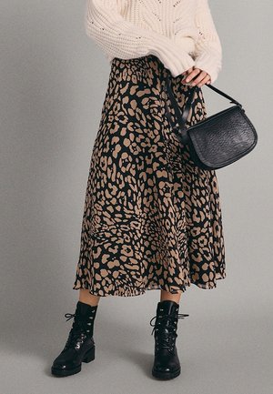 Leopard print midi skirt in black and tan, made of lightweight fabric, paired with black lace-up boots and a textured black shoulder bag.