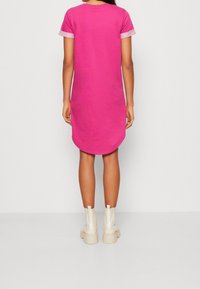Różowa bawełniana sukienka z krótkim rękawem i zaokrąglonym dołem, z kontrastowym jasnoróżowym wykończeniem rękawów. Noszona z białymi, masywnymi botkami za kostkę.