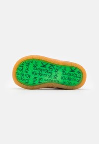 Semelle en caoutchouc verte avec des motifs circulaires, texte "Kickers" et bord de couleur beige ; surface texturée pour une meilleure adhérence.