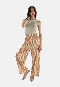 Beige tanktop gecombineerd met losse, gestreepte broeken in oranje en witte tinten, met een elastische tailleband en een strikdetail. Beige schoenen.