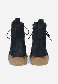 Botas de ante azul marino hasta el tobillo con una suela de plataforma texturizada, que cuentan con un cierre de cremallera y cordones opcionales en la parte trasera para un ajuste ajustable.
