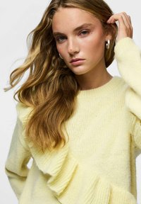 Żółty sweter dziany z falbanką po boku i zaokrąglonym dekoltem. Miękka tekstura o casualowym kroju.