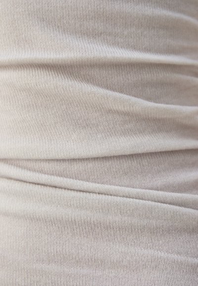 Beige tyg med en ribbad struktur, som visar mjuka veck och draperingar, vilket indikerar ett stretchigt och lätt material.
