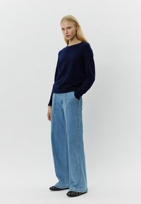 Mornarica pulover, opuštenog kroja, uparen s širokim svijetloplavim trapericama. Crne balerinke sa srebrnim zakovicama upotpunjuju izgled.