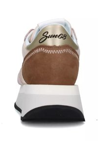 Sneaker con un inserto dorato sul tallone, parte superiore in suede rosa chiaro e mesh, suola intermedia bianca e suola in gomma nera con dettagli di cucitura visibili.