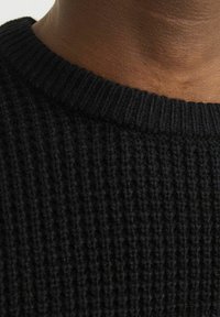 Czarny sweter dziany z teksturą prążkowaną i okrągłym dekoltem, podkreślający miękką tkaninę i zbliżenie na szczegóły obszycia.