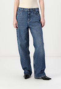 Τζιν παντελόνι μπλε, ψηλόμεσο με φαρδιά μπατζάκια και πέντε τσέπες. Διαθέτει κλασικό κούμπωμα με κουμπί και φερμουάρ, και ελαφρύ ξεθώριασμα για υφή.