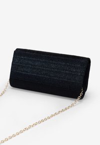 Bolso de mano negro con un diseño de tejido texturizado, forma rectangular y una cadena dorada para llevar. Presenta un interior suave.